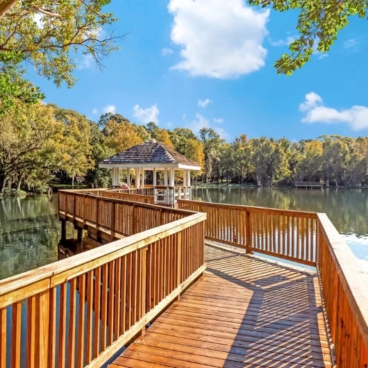 Boardwalk leading to gazebo and fishing area surrounded by beautiful, bright greenery and clear blue skies.